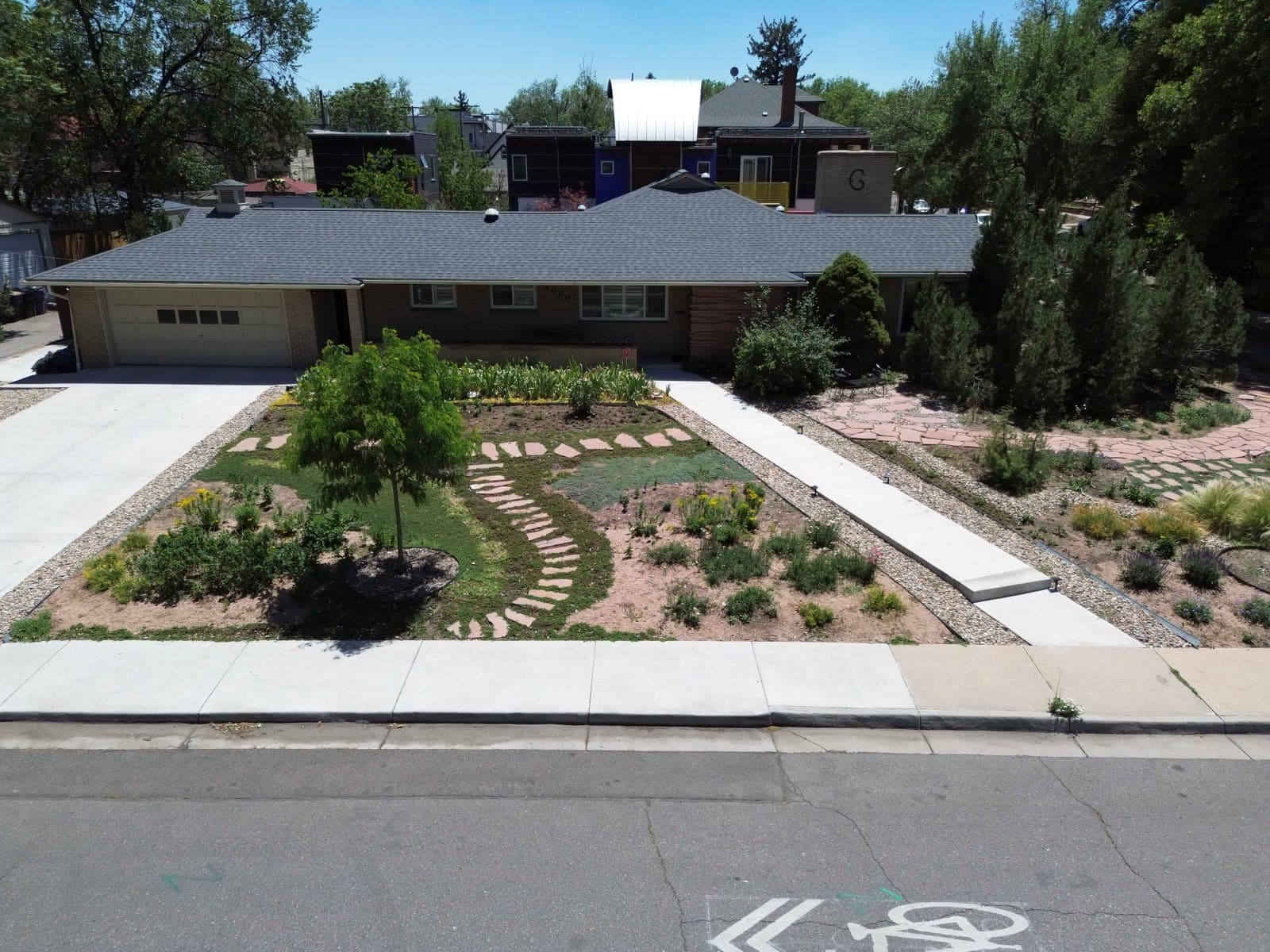 Elevated front view with blonde brick, the attached garage, and terraced garden beds