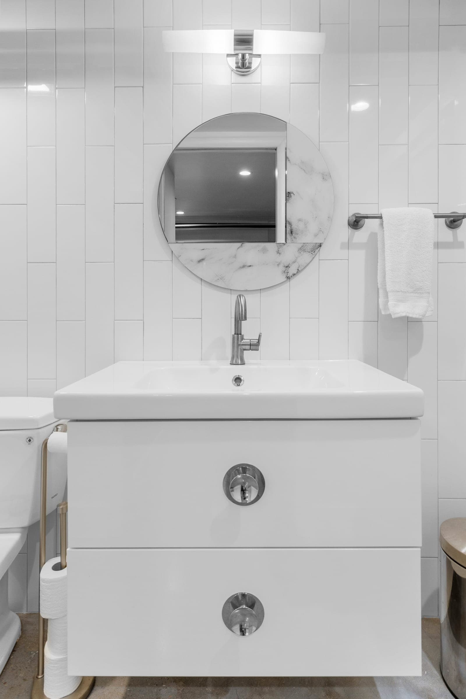 Compact floating vanity with a round marble-edged mirror and vertical stacked tile