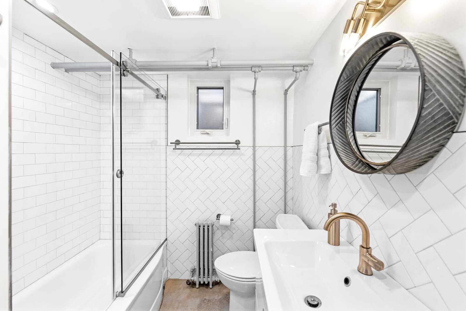 Hall bath with a glass-enclosed tub shower, herringbone tile wainscot, and brushed nickel faucet