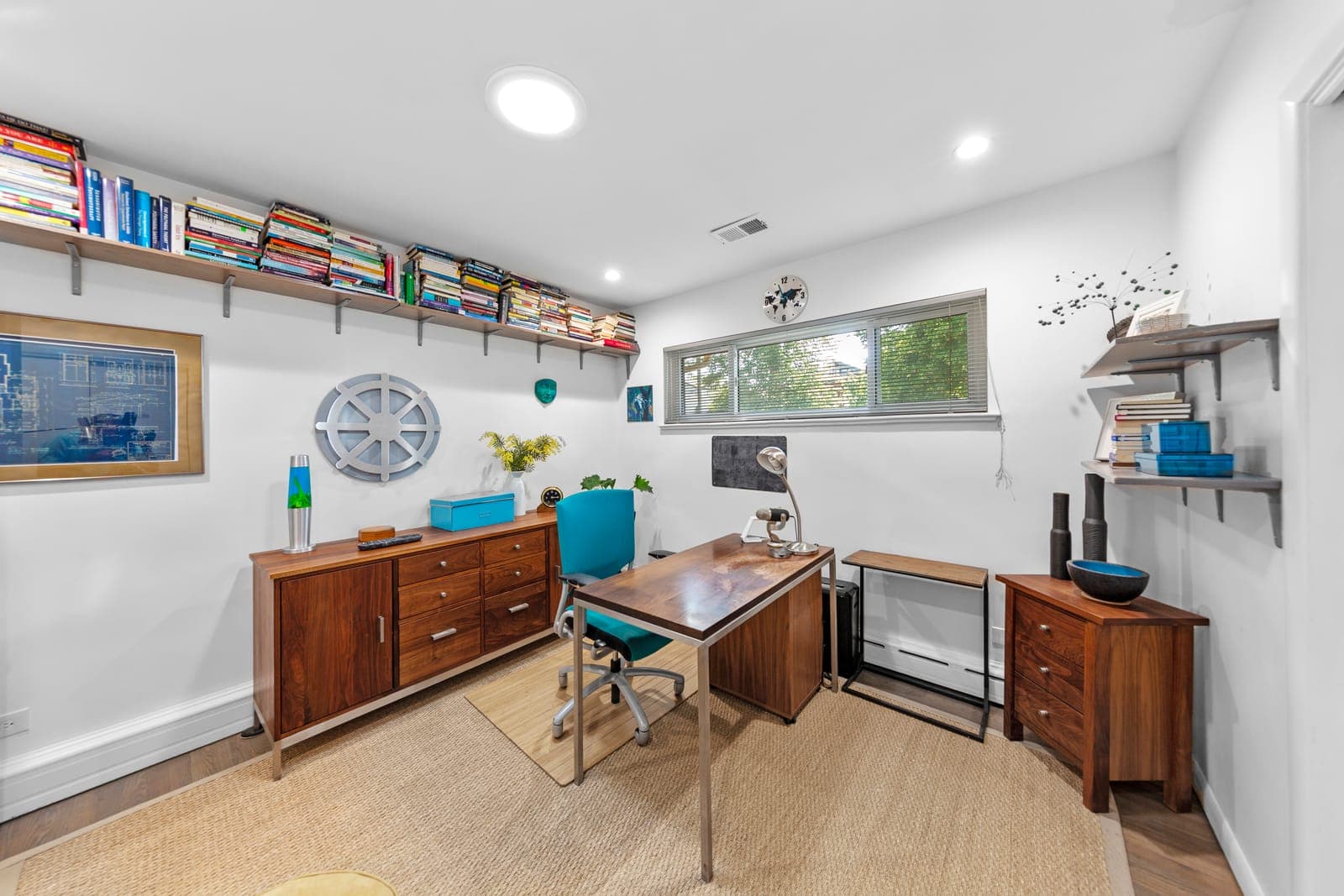 Bedroom staged as a home office with corner shelving, dresser, and framed blueprint art