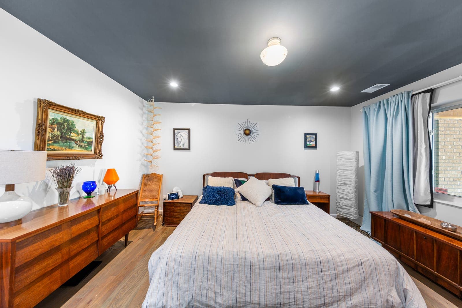 Primary suite bedroom with walnut dressers, a charcoal accent ceiling, and a starburst wall sculpture