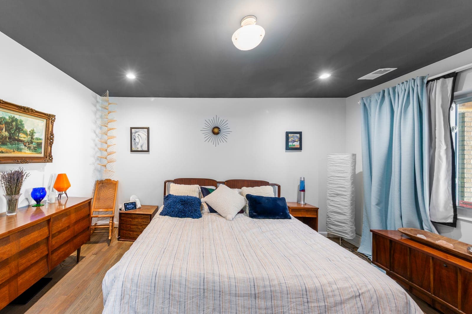 Primary suite bedroom with dark ceiling, mid-century dressers, and glass block window