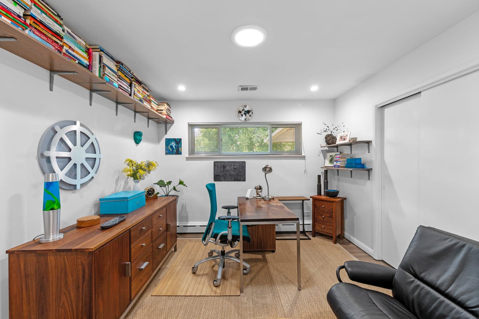 Bedroom staged as a home office with walnut credenza, wall-length book shelving, and desk