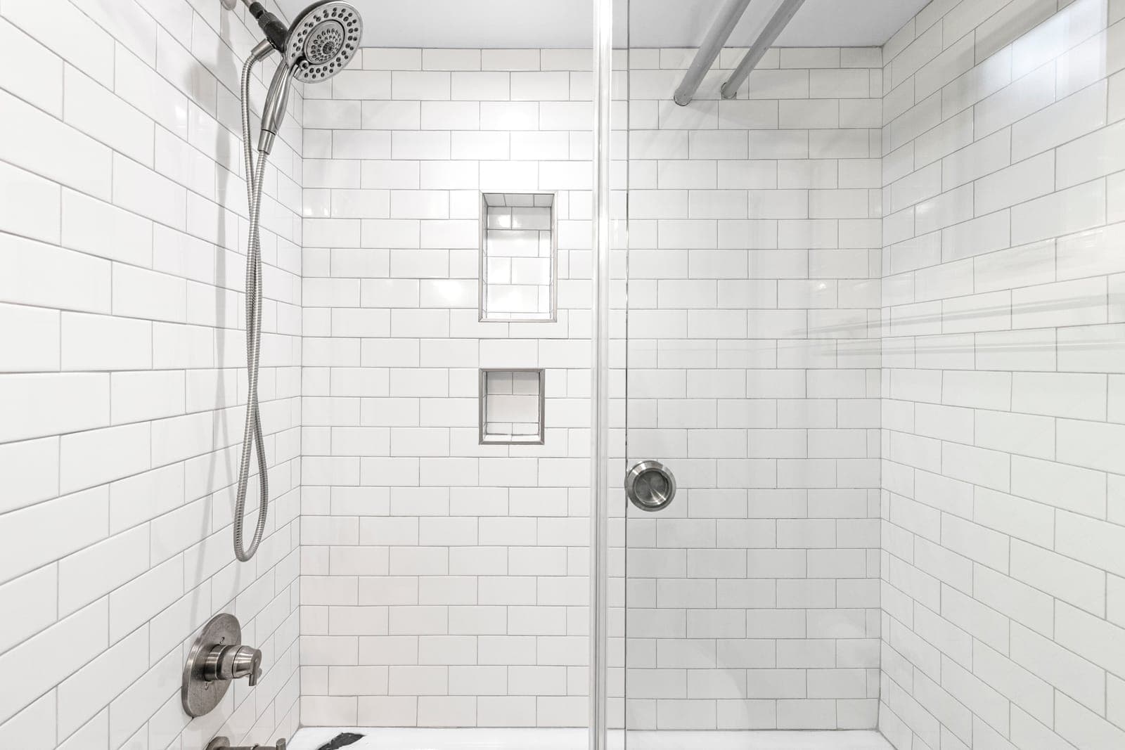 Tub shower in white subway tile with two recessed niches and a handheld shower head