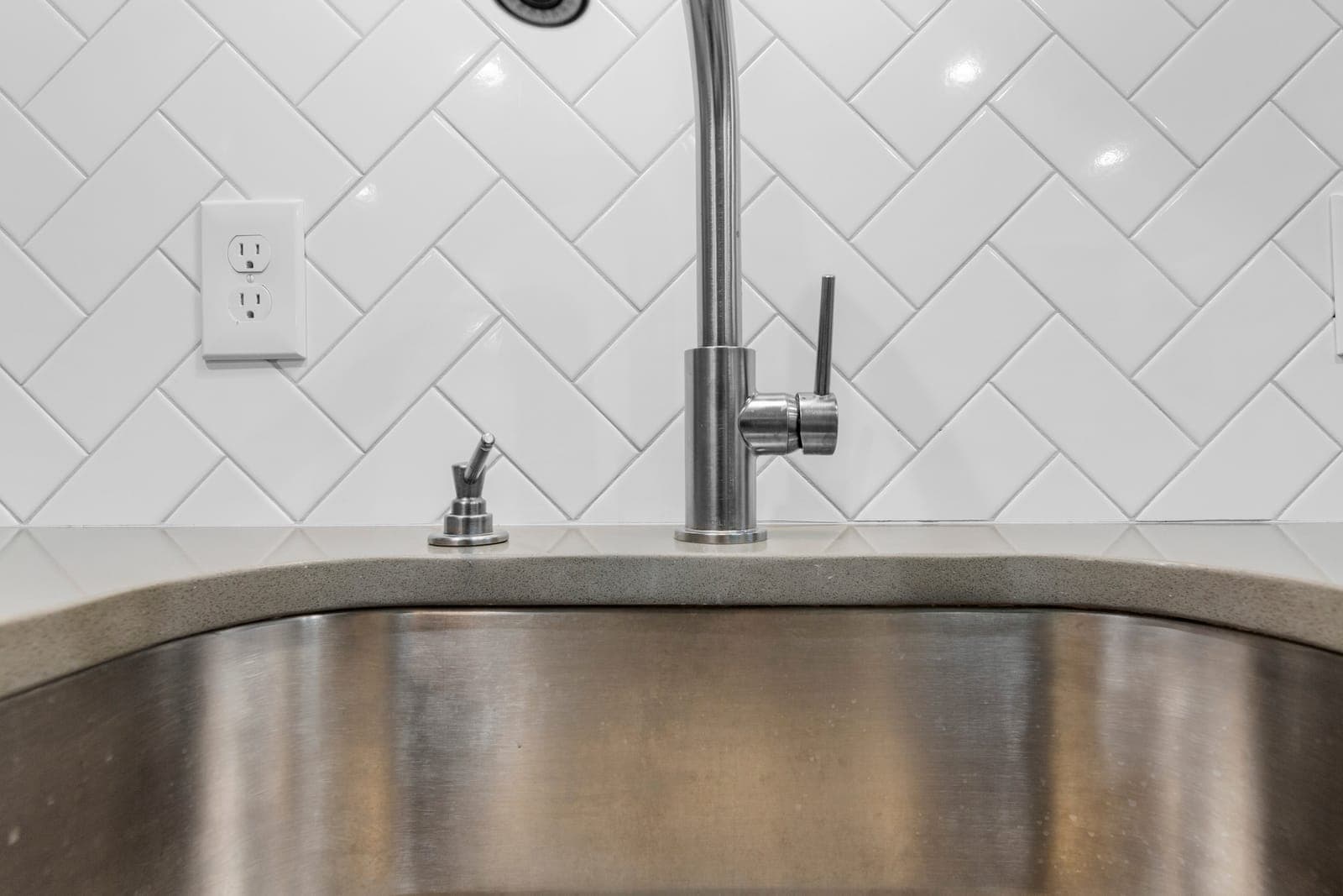 Kitchenette sink detail with herringbone tile and a stainless gooseneck faucet