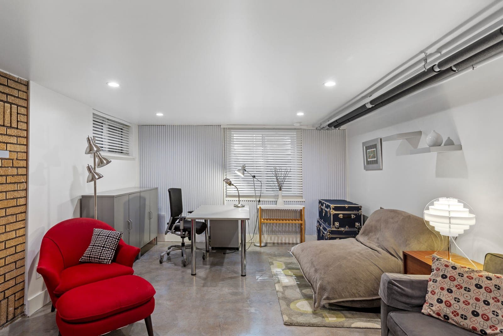 Lower-level lounge corner with a red armchair, desk area, and daybed
