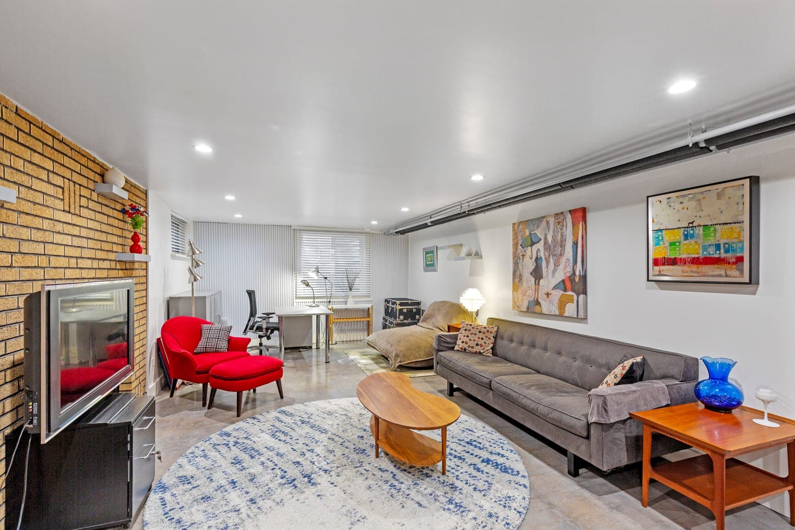 Lower-level sitting area with a grey tufted sofa, red wingback chair, and gallery art wall