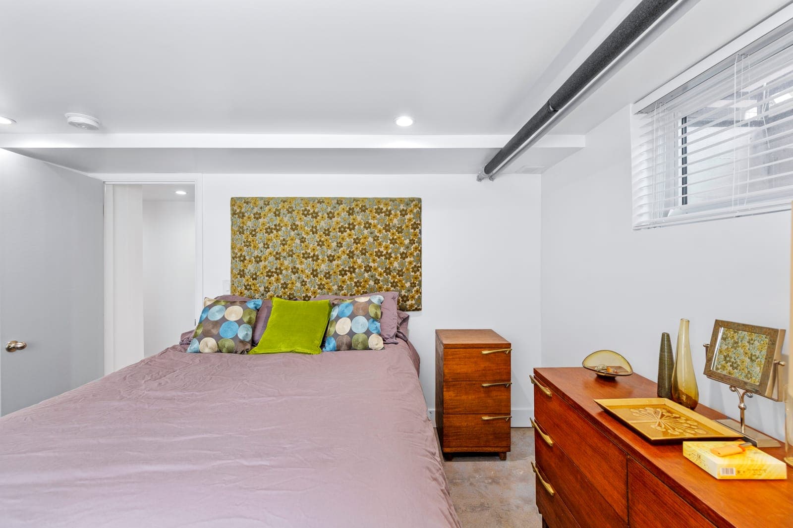 Lower-level bedroom with walnut dressers, a mid-century chest, and vintage accents