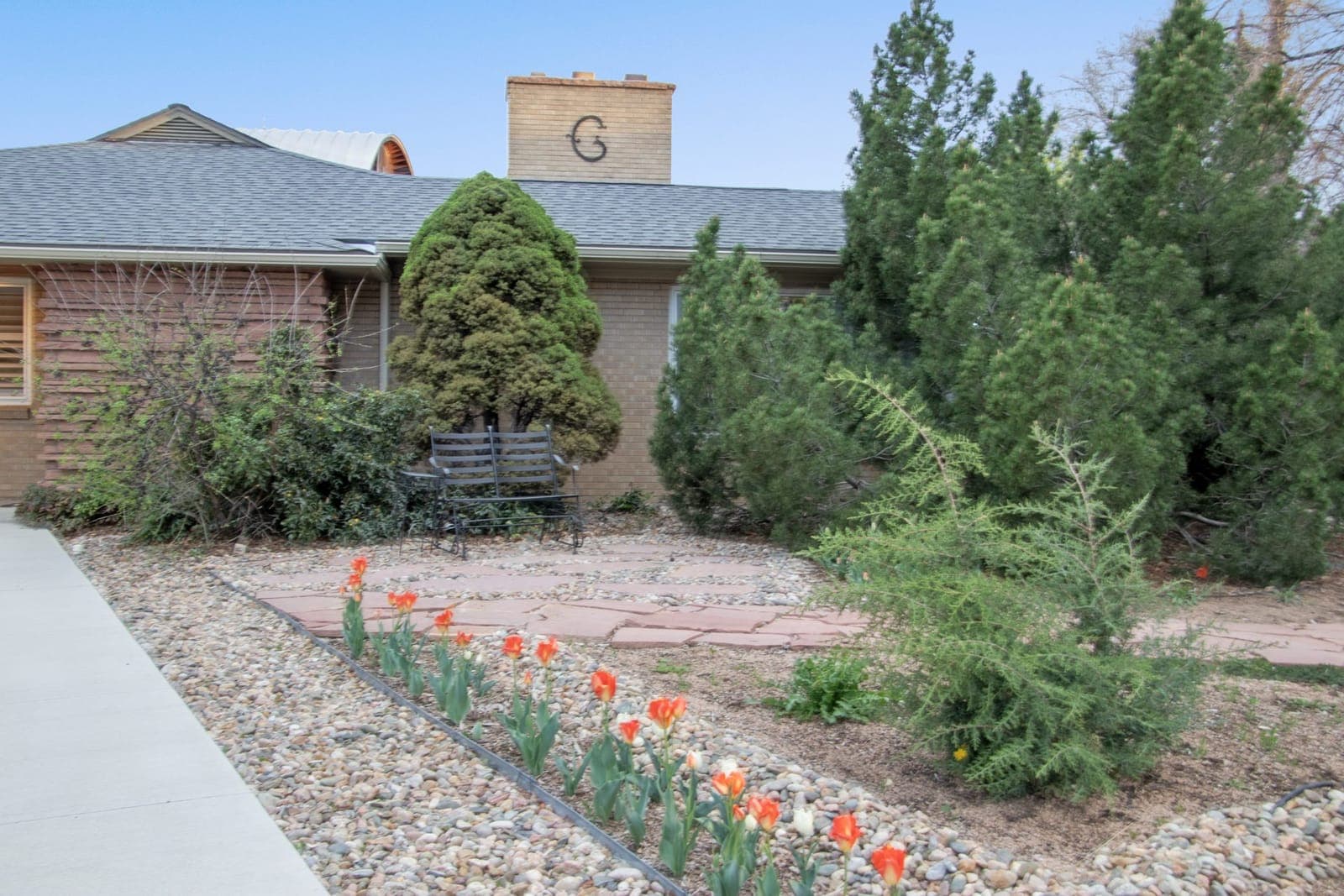 Front sitting area framed by evergreen shrubs, with tulips along the rock border