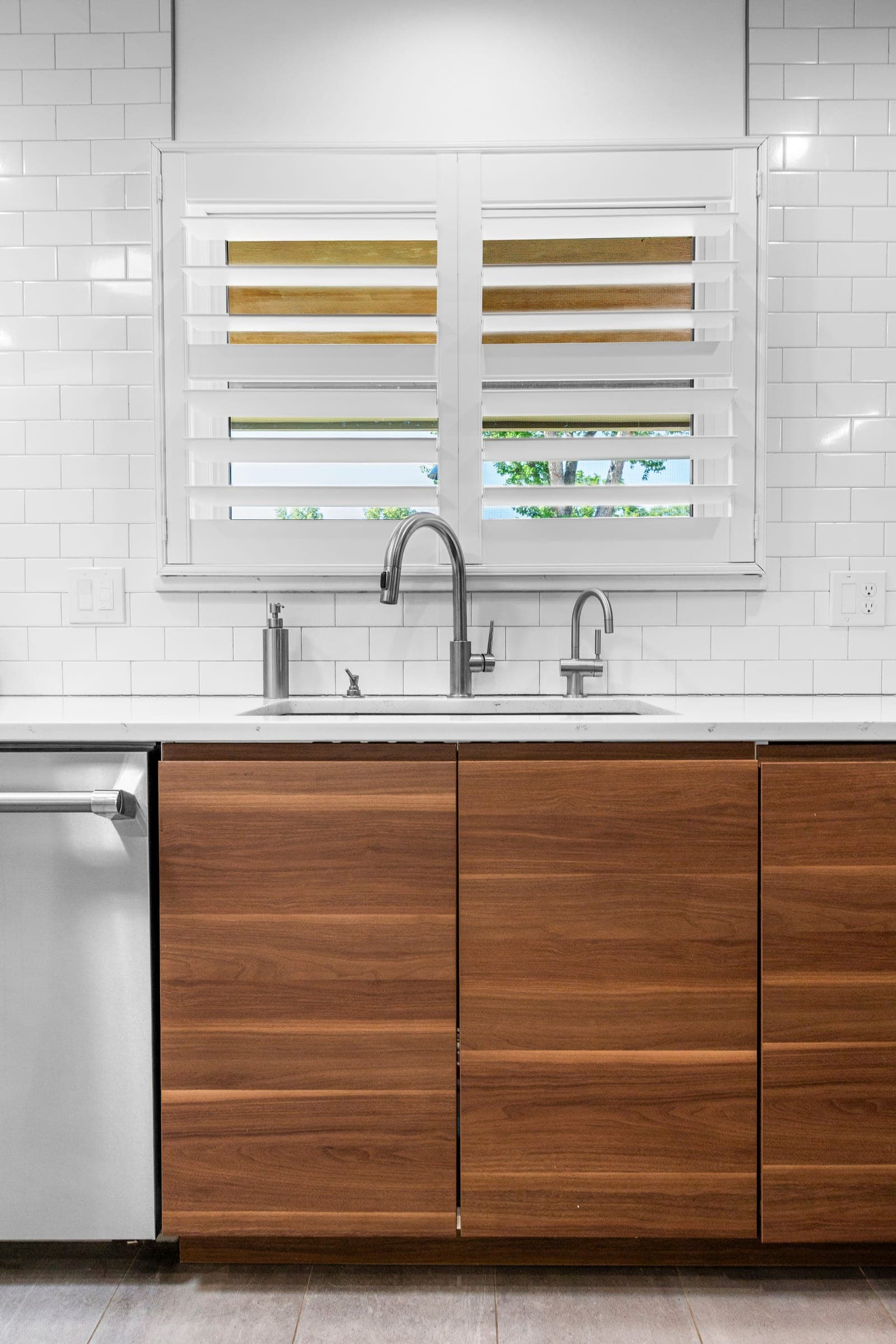 Kitchen sink wall with walnut cabinetry, white quartz counters, and plantation shutters