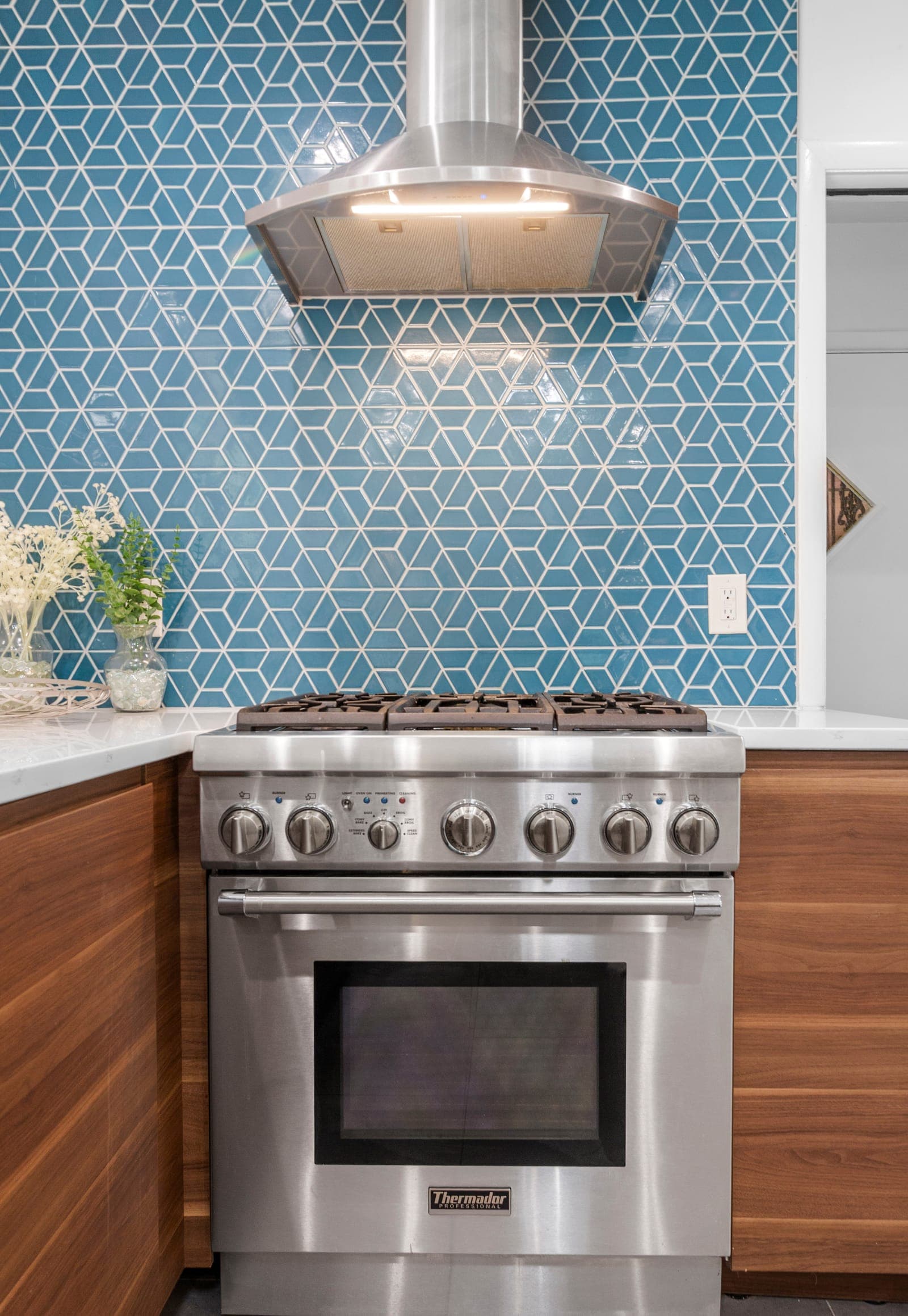Professional gas range and chimney hood framed by the blue geometric tile wall