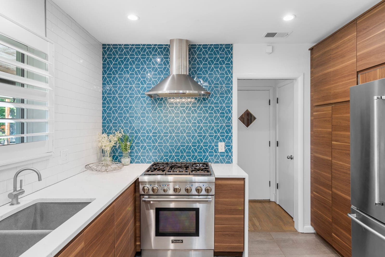 Gas range and stainless chimney hood set against the blue geometric tile backsplash