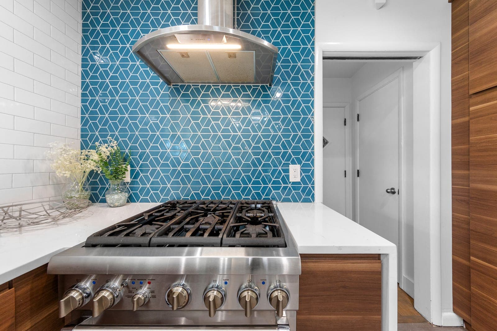 Six-burner gas range and vent hood set against blue geometric tile and walnut cabinetry