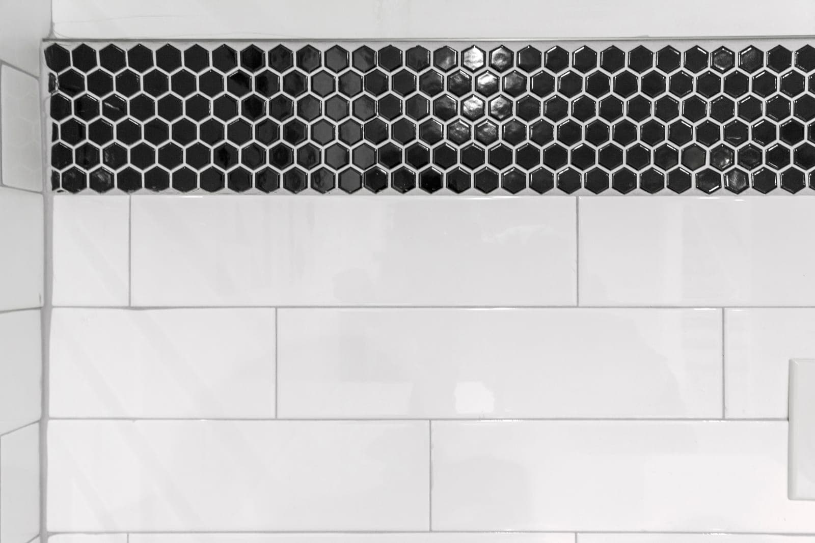 Shower accent band of glossy black hexagon mosaic set into white subway tile