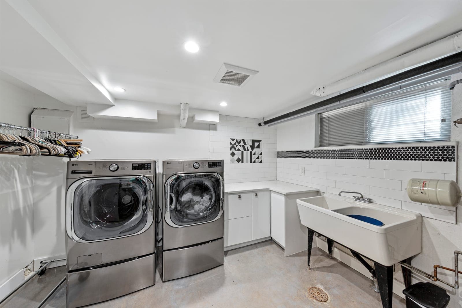 Laundry room with side-by-side front-load machines, a utility sink, and a black mosaic accent stripe