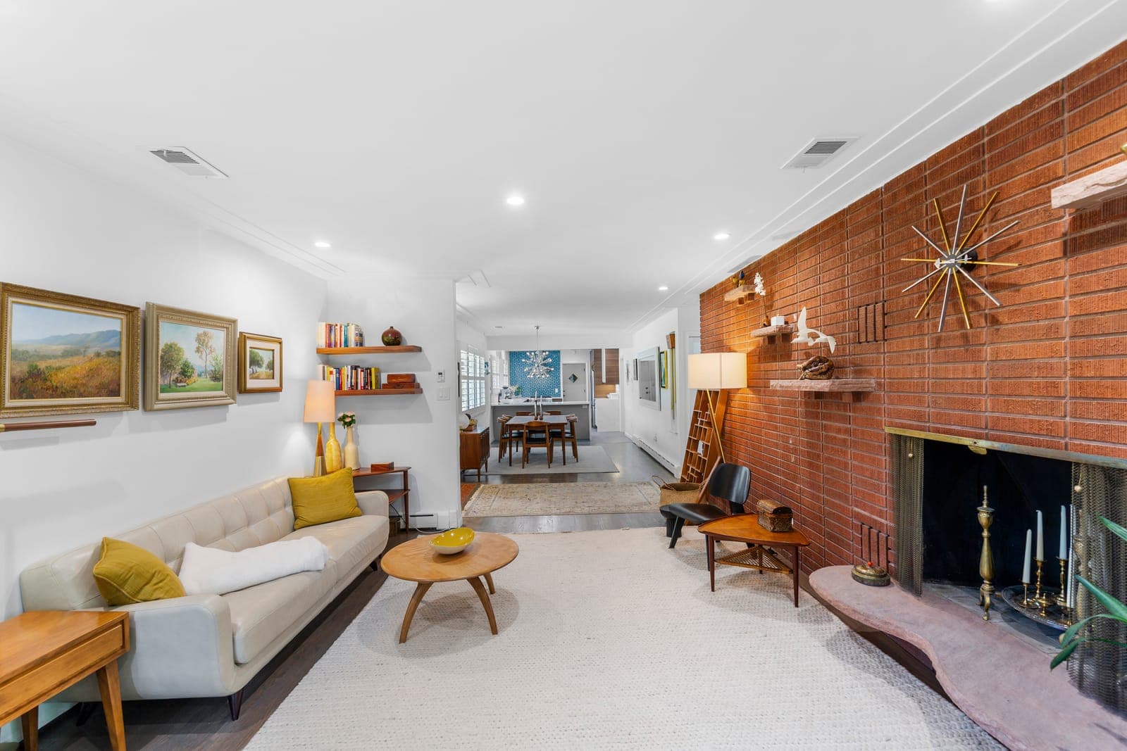 Open living room flowing toward the dining room and kitchen along the brick fireplace wall