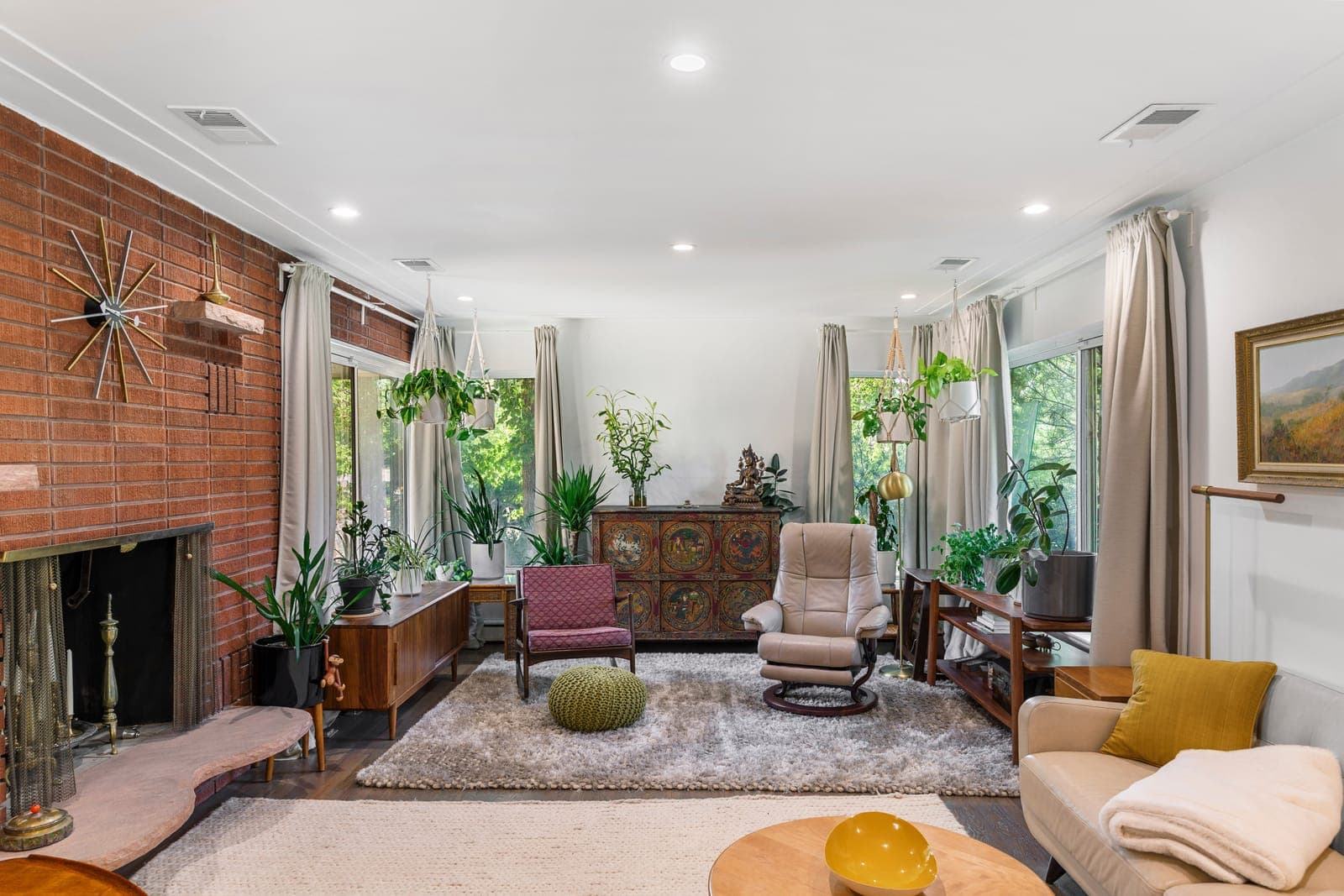 Bright living room with corner windows, a brick fireplace wall, and a starburst clock