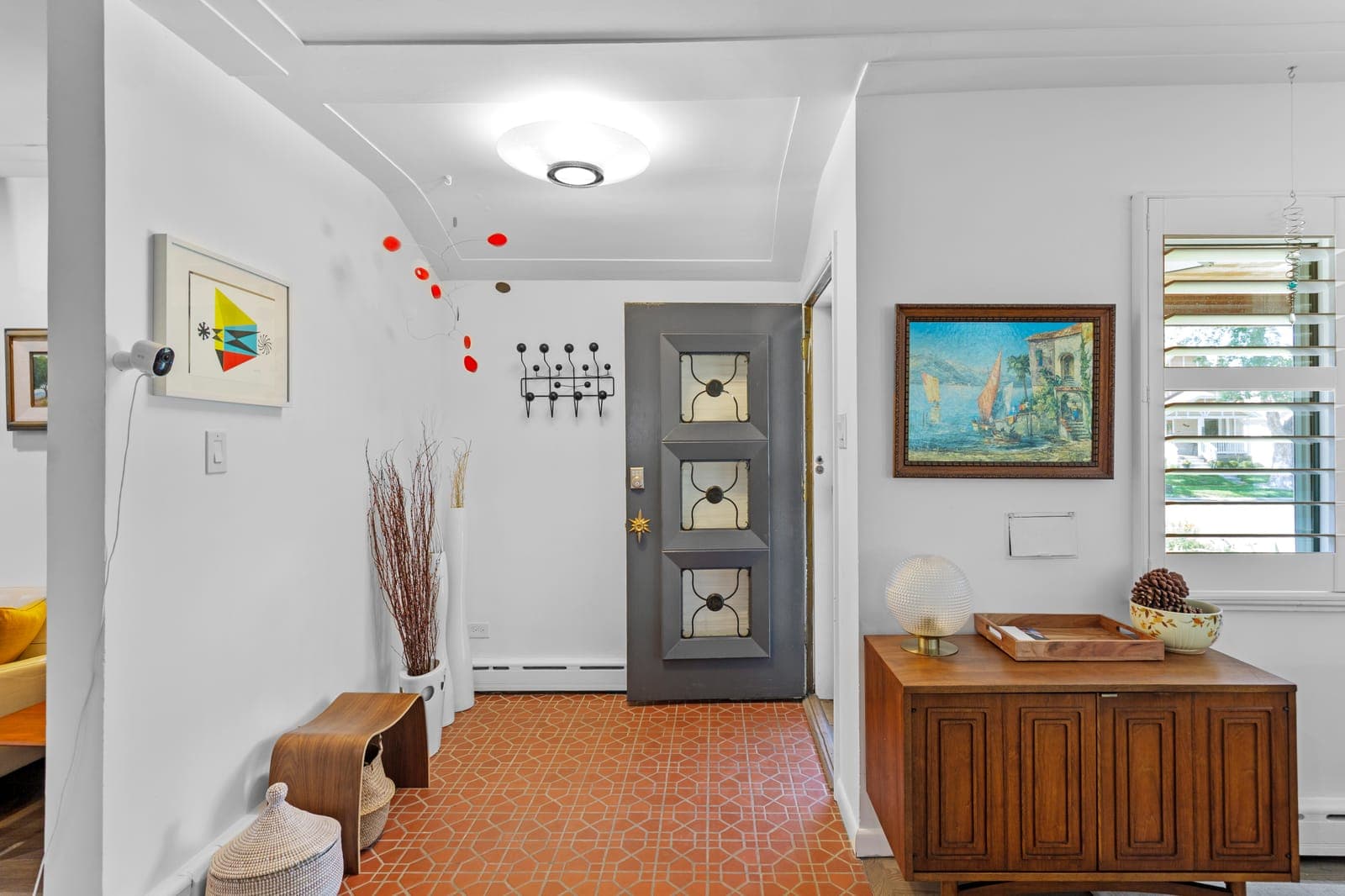 The entry foyer with original tile floor, mid-century credenza, and hairpin coat rack