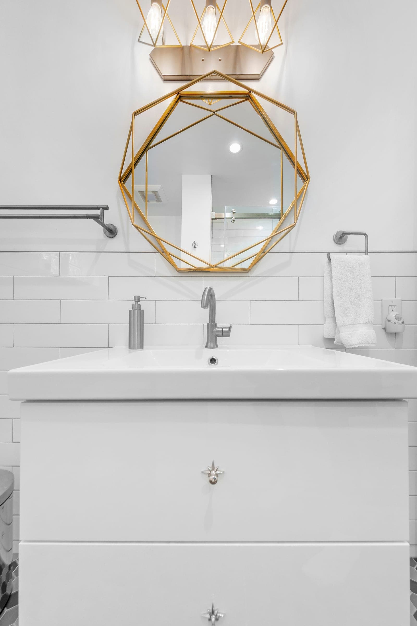 White vanity with geometric gold mirror and subway tile