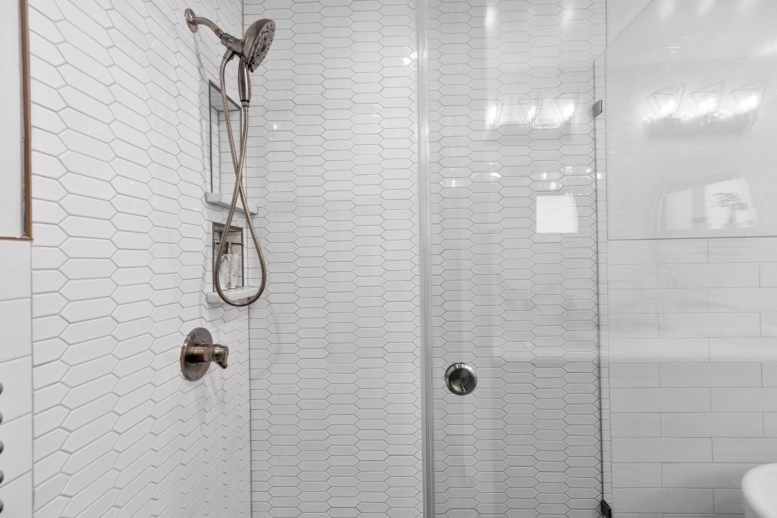 Walk-in shower detail with white picket tile, a recessed storage niche, and a brushed-nickel handheld fixture