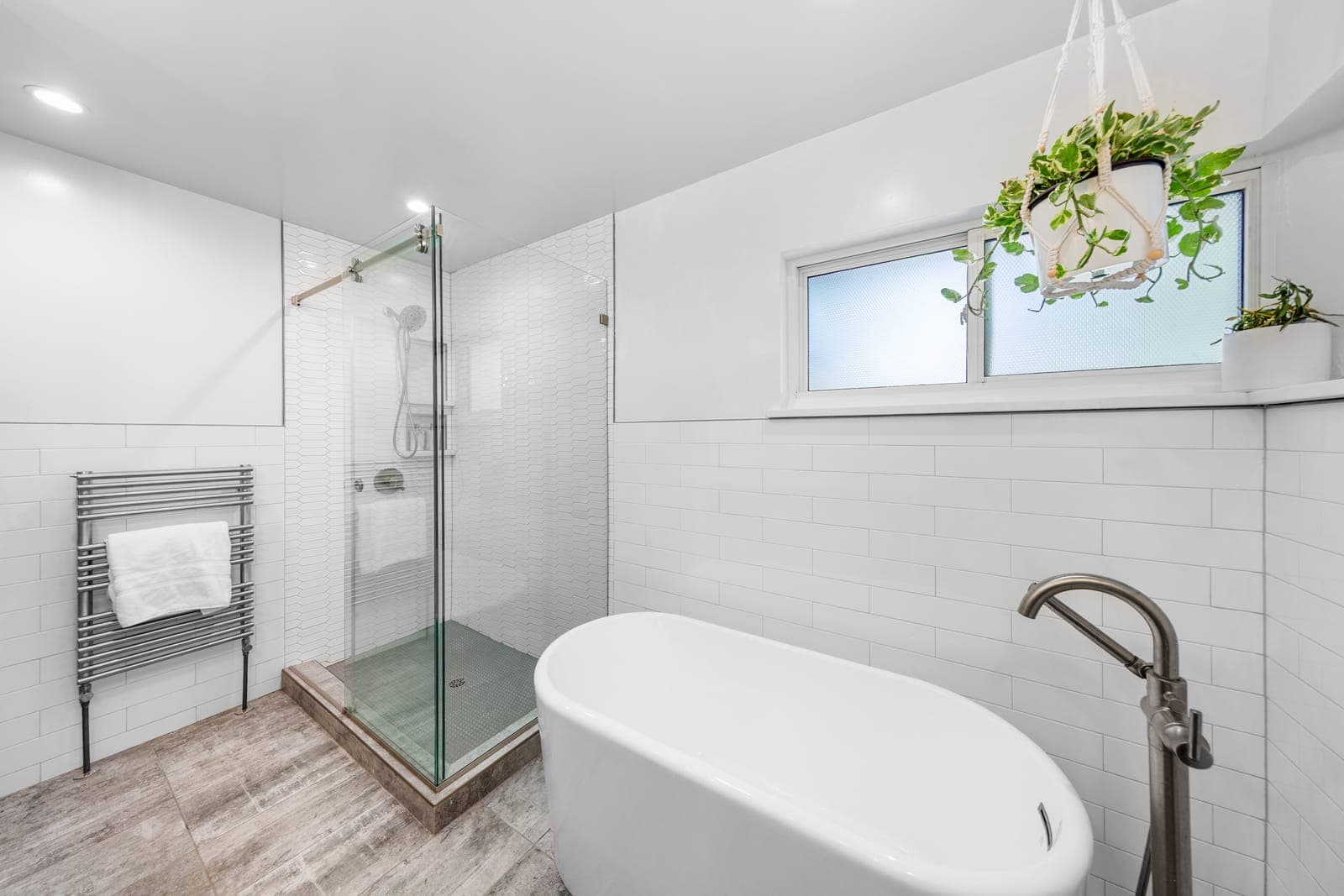 Freestanding soaking tub with a floor-mounted filler, glass-enclosed picket-tile shower, and heated towel rack