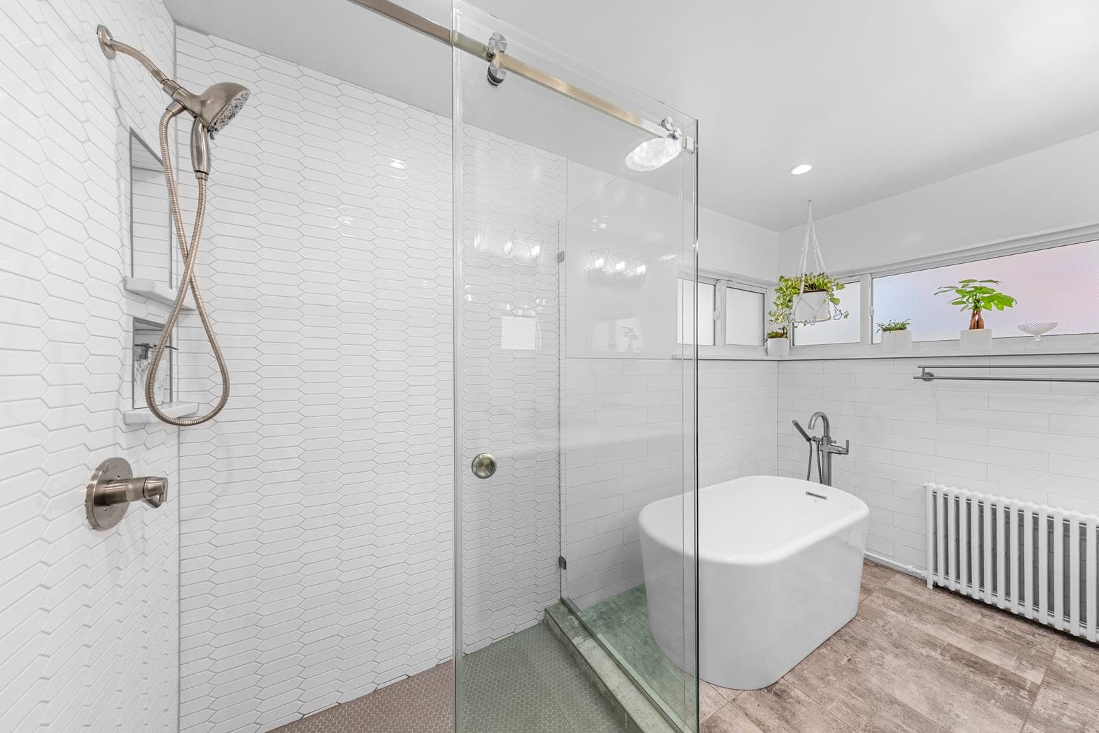 Glass-enclosed walk-in shower in white picket tile beside the freestanding soaking tub