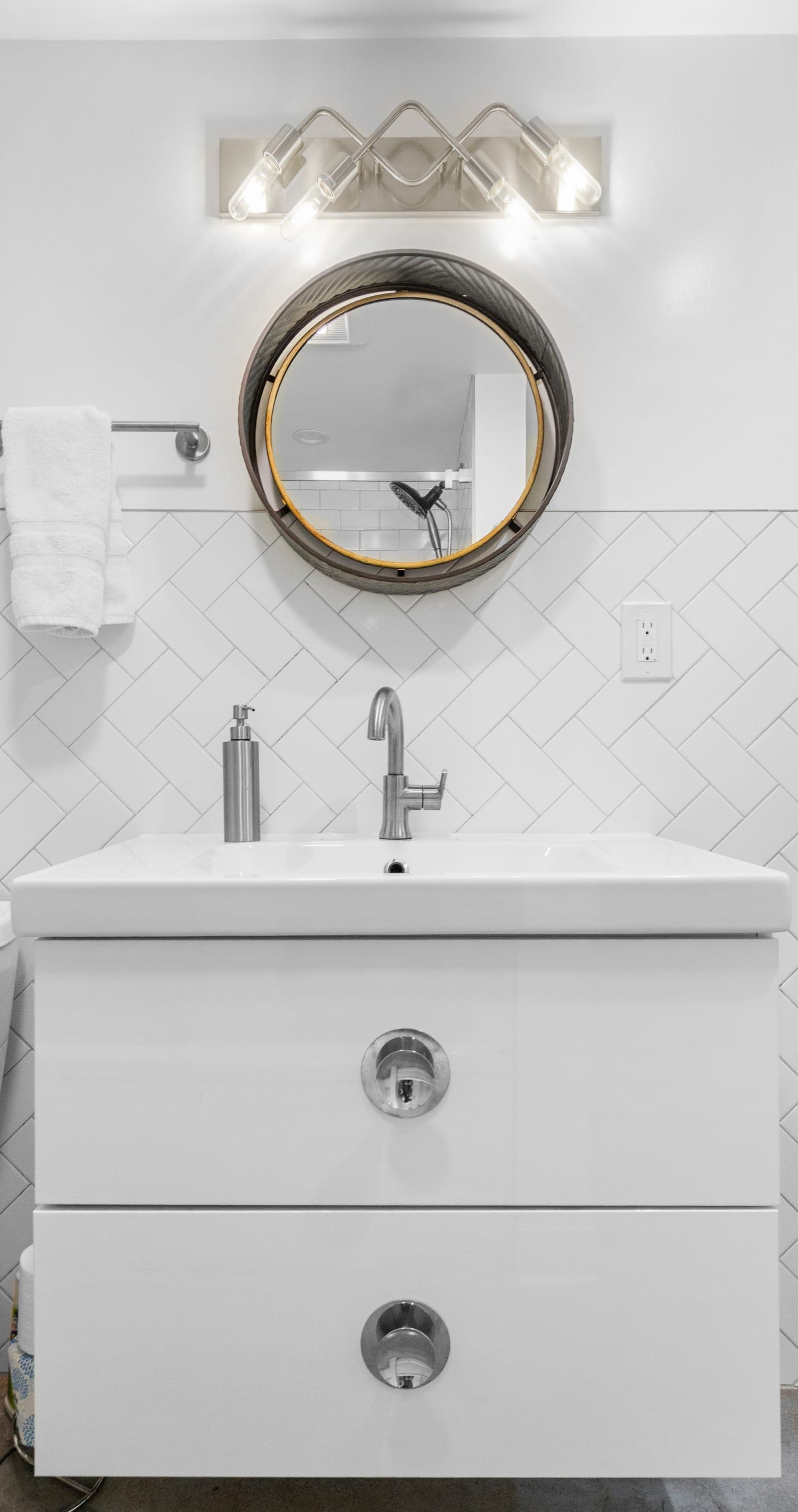 Guest bath vanity with round metal-framed mirror and herringbone tile