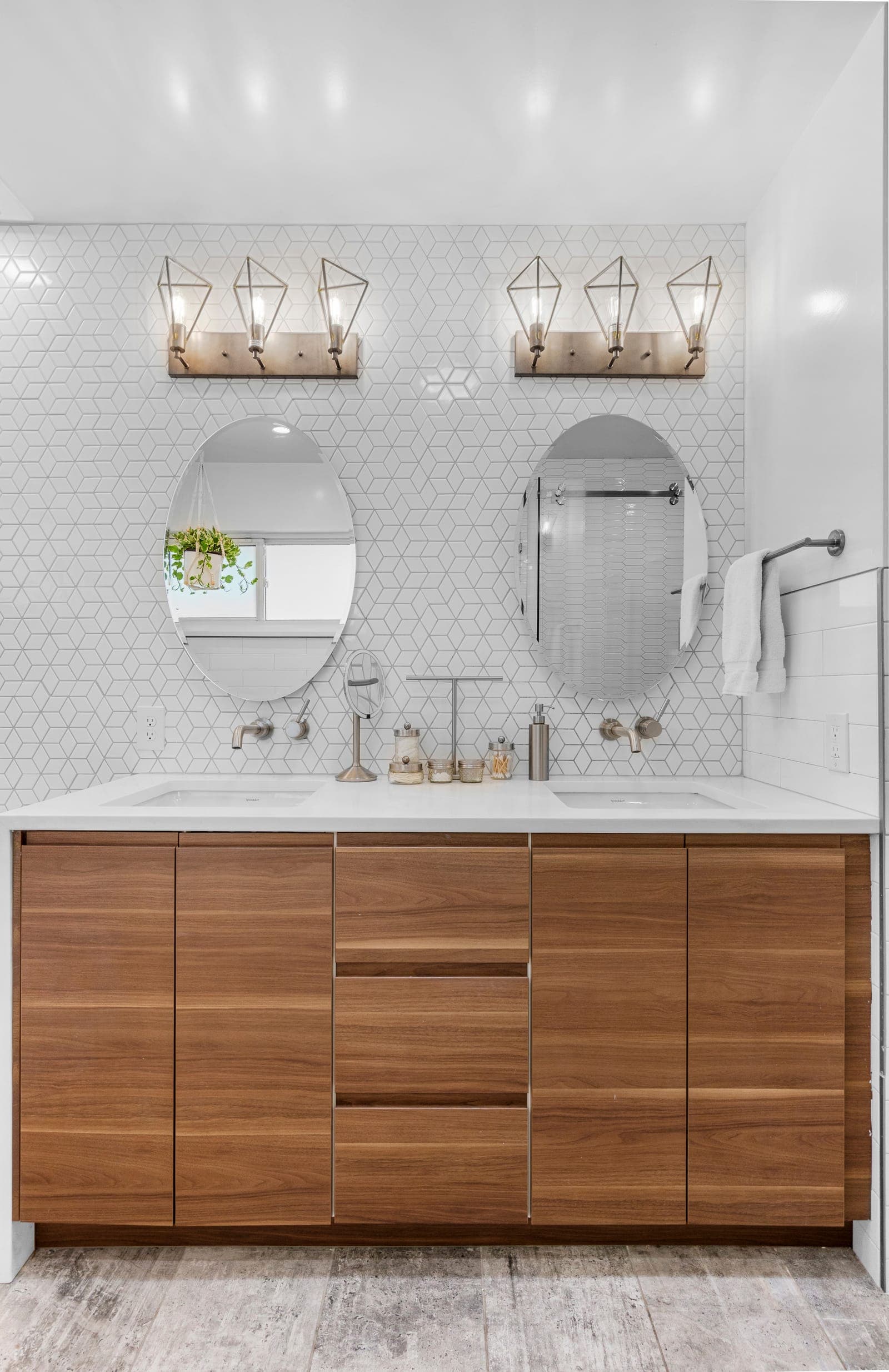 Primary bath walnut double vanity with oval mirrors and diamond mosaic tile wall