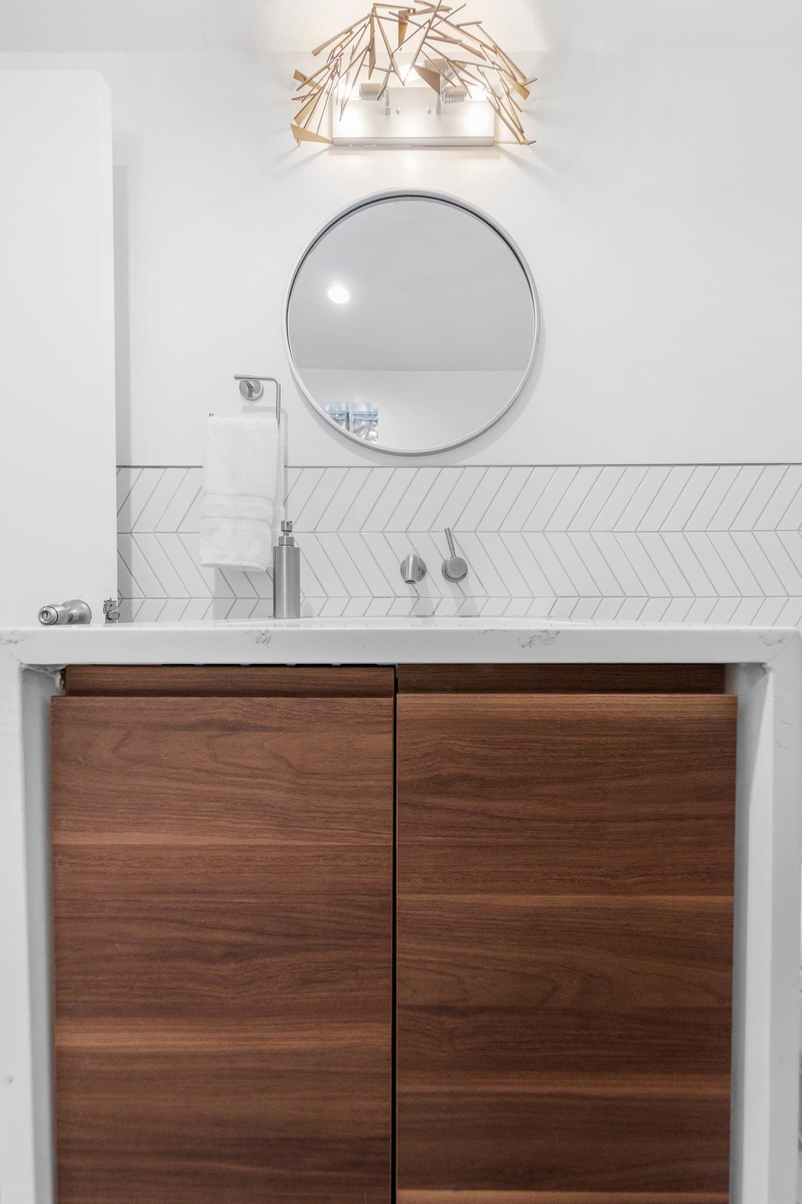 Walnut powder bath vanity with quartz counter, wall-mounted faucet, and chevron tile