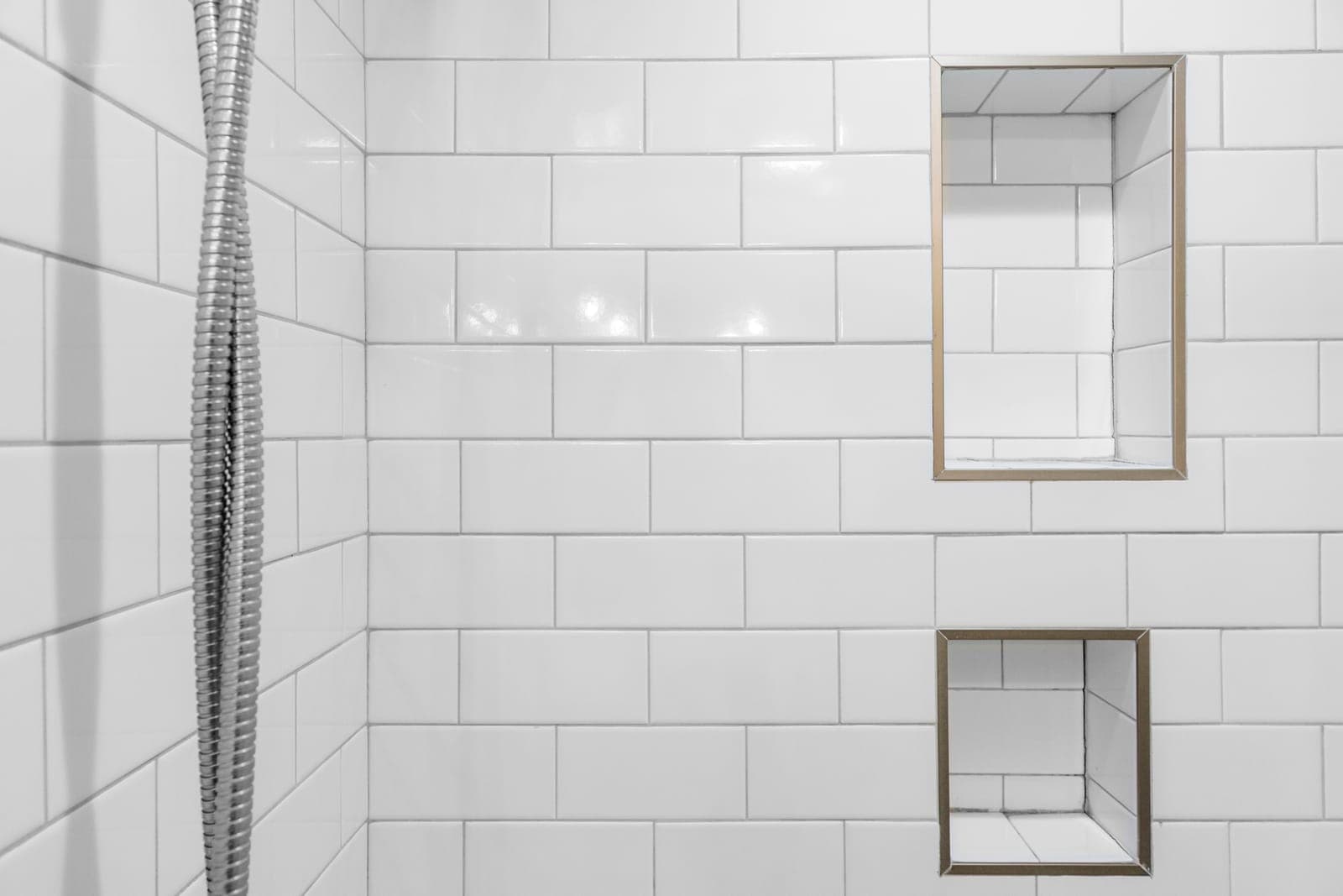 Walk-in shower wall in white subway tile with two recessed storage niches