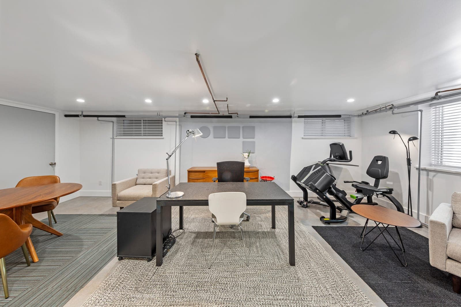 Lower-level flex space with a desk, lounge chair, and exercise equipment