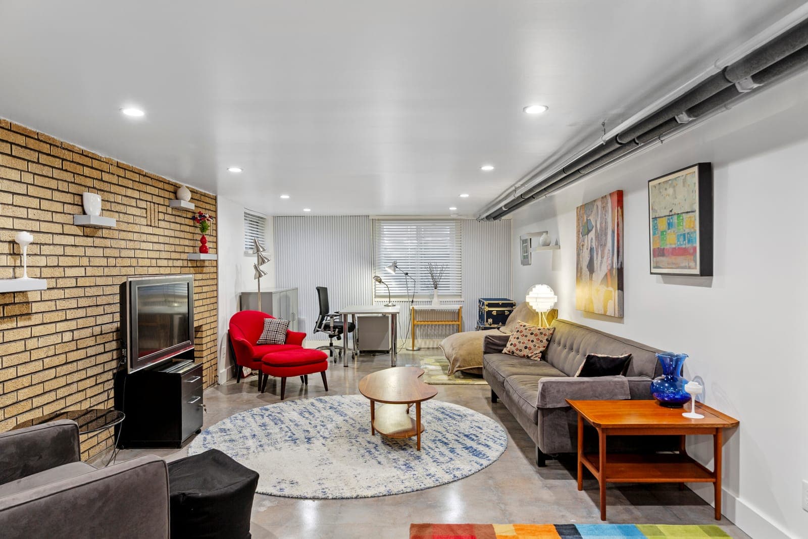 Lower-level lounge with a blonde brick fireplace wall, floating shelves, and a media area