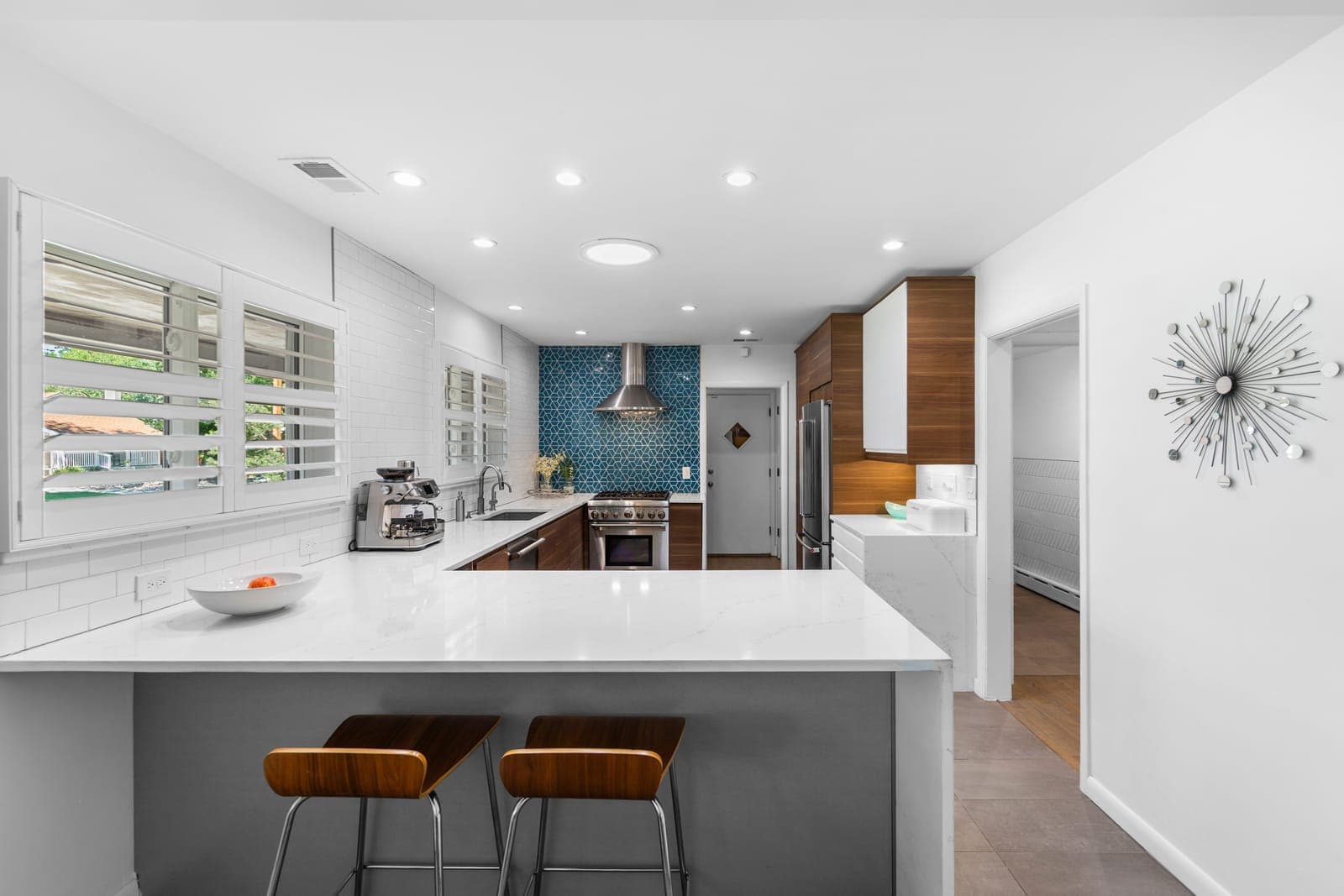 Kitchen peninsula with quartz counters, walnut bar stools, and a blue geometric tile backsplash