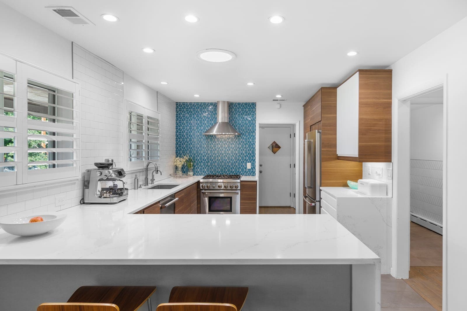 Kitchen with walnut cabinetry, quartz peninsula, and a stainless hood over blue geometric tile