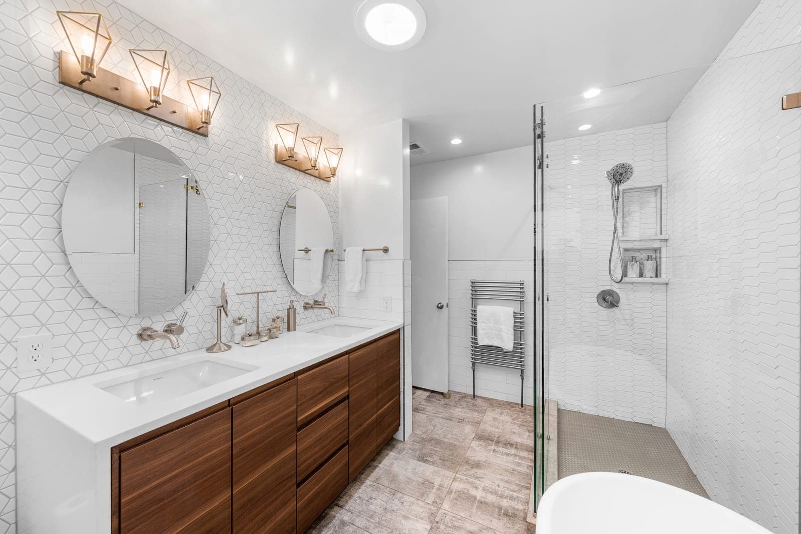 Double vanity with a floating walnut cabinet, round mirrors, and brushed nickel geometric sconces beside the walk-in shower