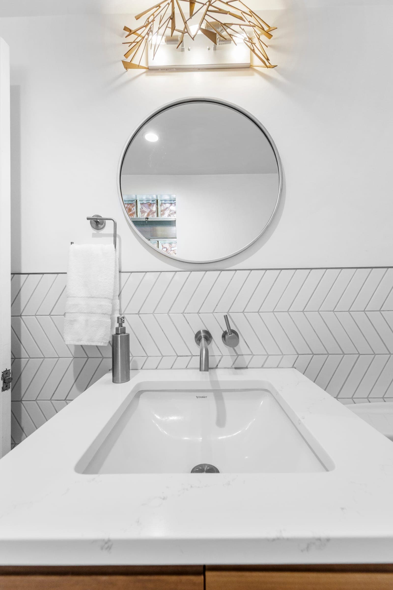 Powder bath vanity with round mirror, sculptural sconce, and chevron tile wainscot